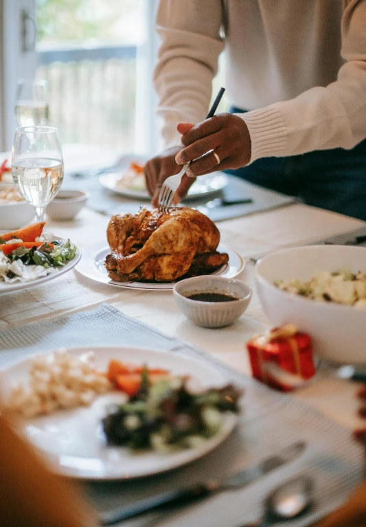 a group of people sitting at a table with plates of food, chicken, holiday vibe, realistic »