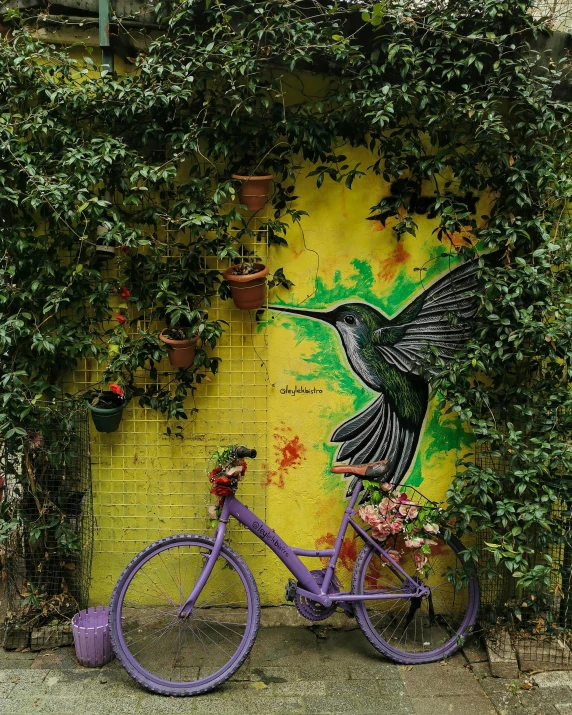 a purple bicycle parked in front of a yellow wall, by Lucia Peka, pexels contest winner, street art, hummingbirds, lush green, spraypainted on a wall, hummingbird