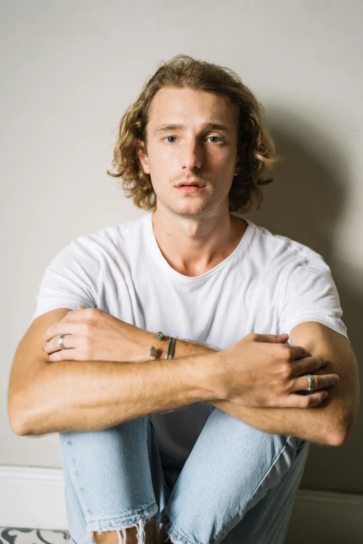 a man sitting on the floor with his arms crossed, an album cover, inspired by Anthony Devas, trending on pexels, young simon baker, well defined jawline, sydney hanson, concert