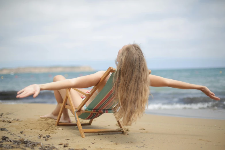 a woman sitting in a chair on the beach, pexels contest winner, pretty face with arms and legs, arms out, naturalistic technique, unwind!