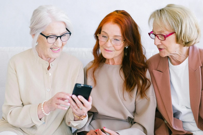 three women sitting on a couch looking at a cell phone, trending on pexels, an old lady with red skin, square rimmed glasses, royal commission, silver haired