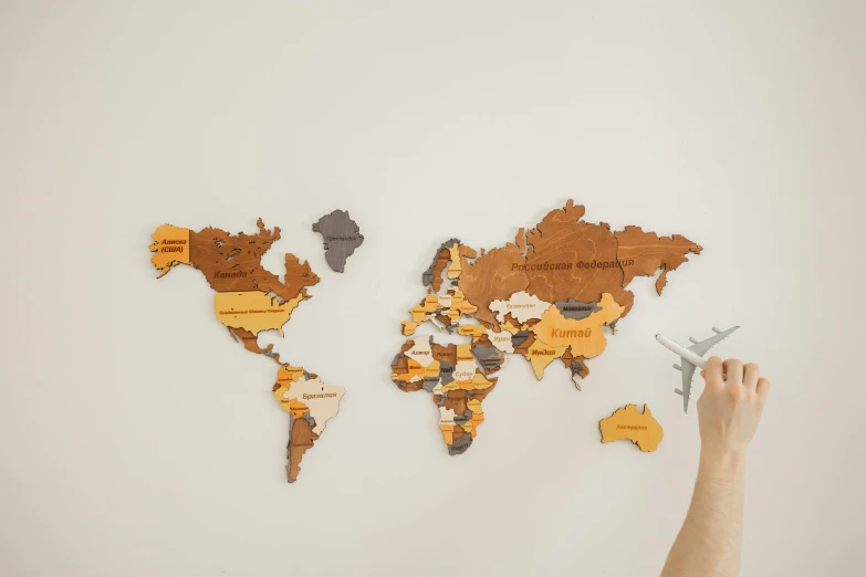 a person holding a toy airplane in front of a map of the world, a jigsaw puzzle, by Will Ellis, pexels, interactive art, wooden decoration, dark grey and orange colours, sculpture made of wood, with names