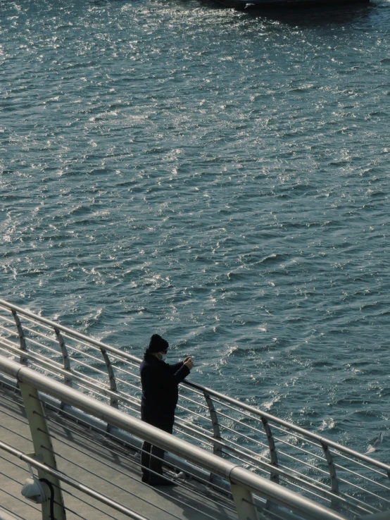 a person standing on a bridge looking at a boat in the water, wavy water, checking her phone, dark ocean water, instagram story