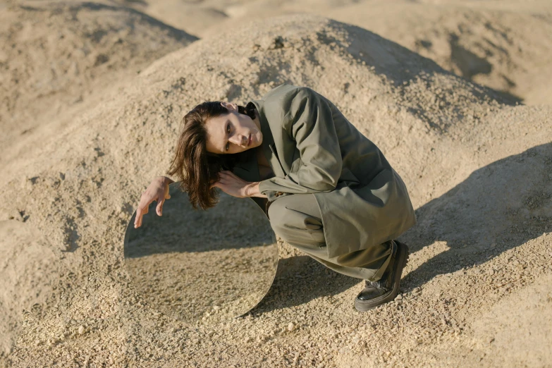 a woman kneeling on top of a pile of sand, wearing human air force jumpsuit, cracked earth, lena oxton, prop rocks