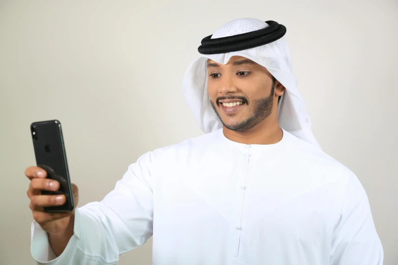 a close up of a person holding a cell phone, inspired by Ahmed Yacoubi, hurufiyya, wearing authentic attire, smiling male, tanned ameera al taweel, light mode