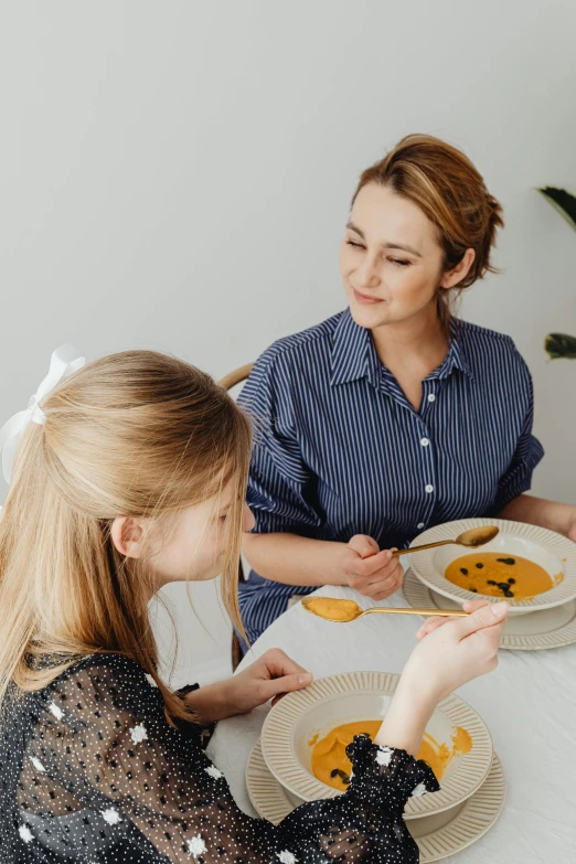 two women sitting at a table with plates of food, pexels contest winner, with a kid, profile image, manuka, slightly minimal