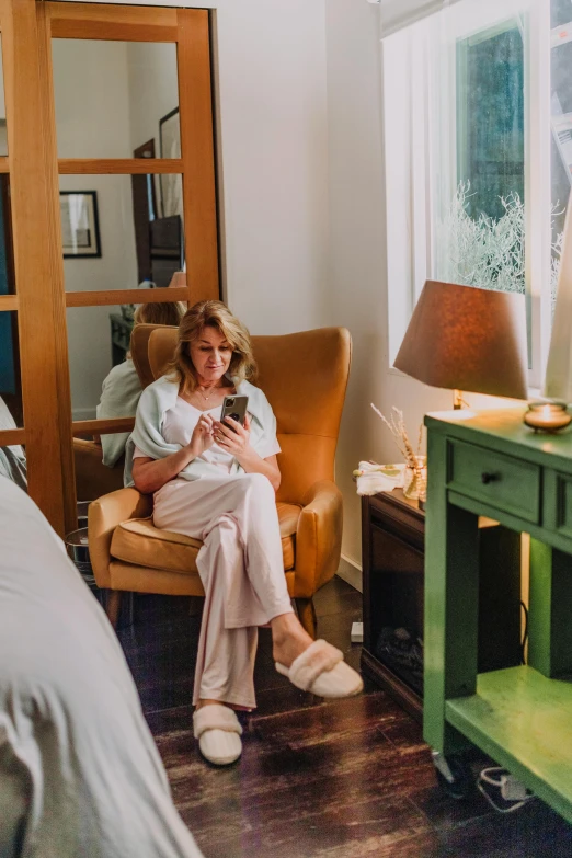 a woman sitting in a chair looking at her cell phone, hygge, hotel room, maternity feeling, 2019 trending photo