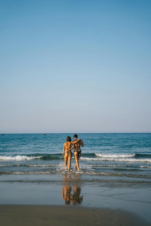 a couple of people standing on top of a beach, unsplash, minimalism, swimming in ocean, lesbians, sunny day time, bum