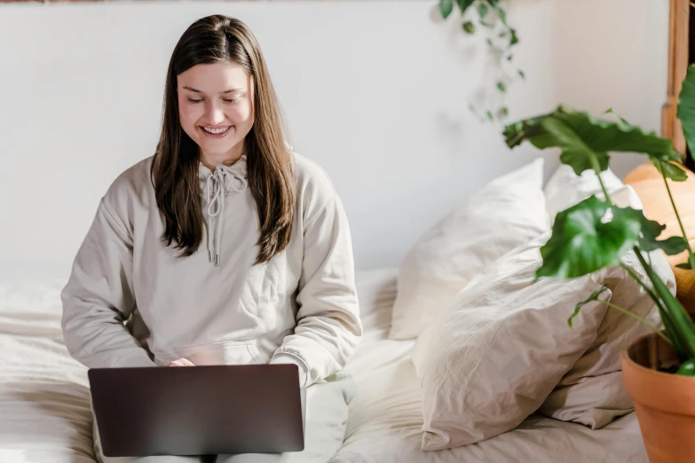 a woman sitting on a bed with a laptop, trending on pexels, girl with brown hair, subject is smiling, avatar image, nursing