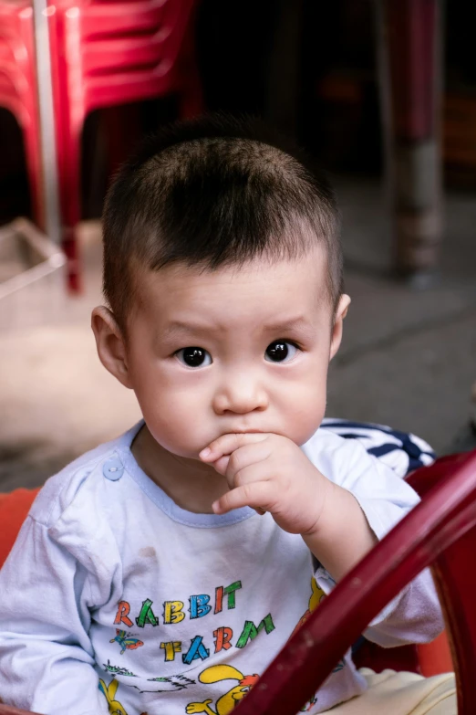 a small child sitting in a red toy car, inspired by Xie Huan, sitting in a cafe, serious focussed look, hand over mouth, square