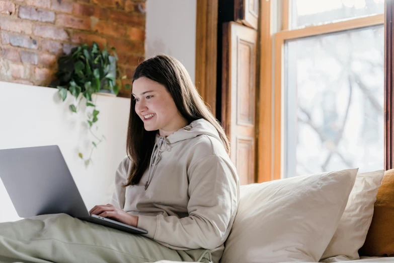 a woman sitting on a bed using a laptop, trending on pexels, at the sitting couch, avatar image, student, brown