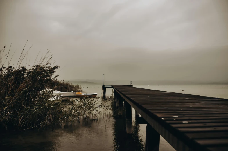 a boat sitting on top of a body of water, inspired by Elsa Bleda, unsplash, boat dock, grey skies rain, the dead sea, autumn rain turkel