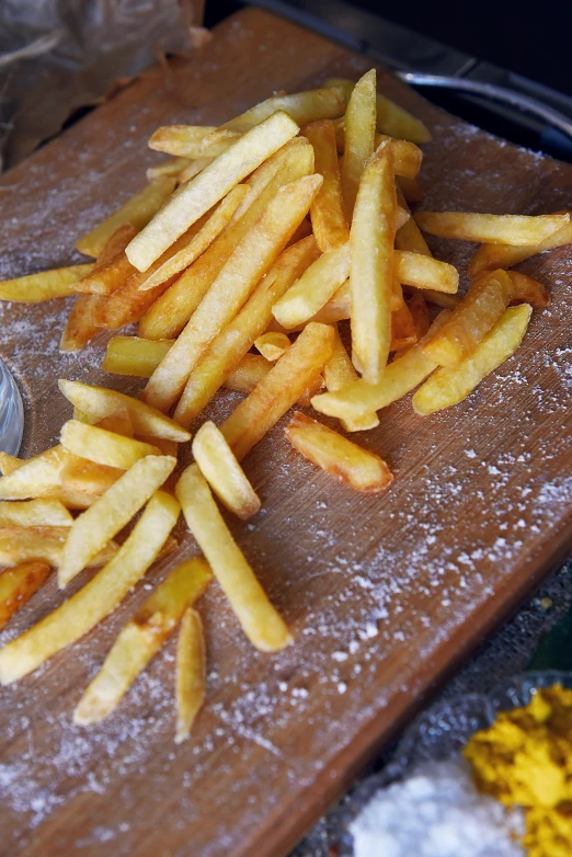 a wooden cutting board topped with french fries, dust, cornwall, stunning quality, chalk