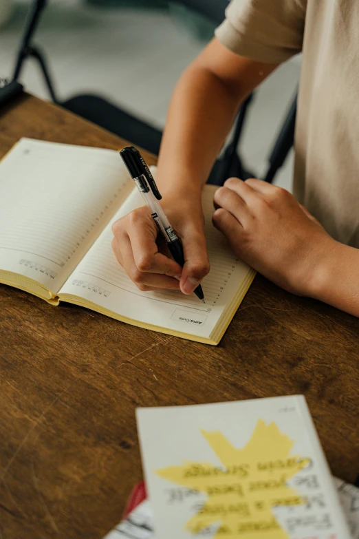 a person sitting at a table writing in a notebook, on a yellow paper, private school, thumbnail, inspect in inventory image