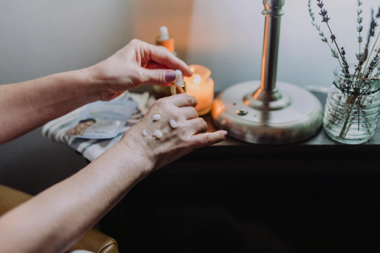 a person lighting a candle on a table, by Emma Andijewska, trending on pexels, skincare, offering the viewer a pill, with crystals on the walls, fan favorite