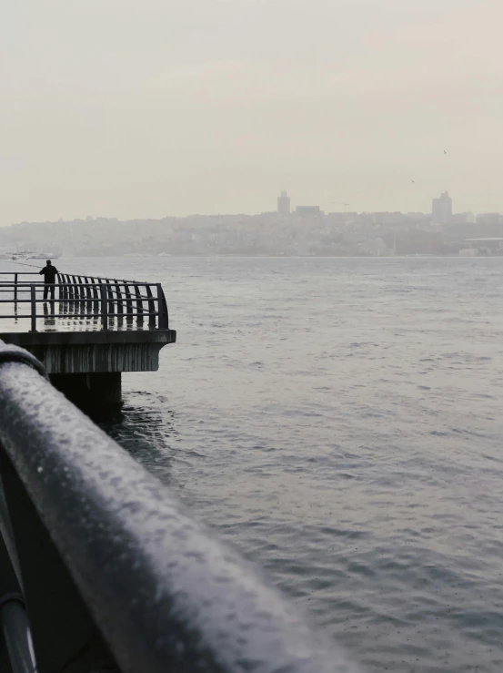 a man standing on top of a pier next to a body of water, inspired by Elsa Bleda, hurufiyya, overcast gray skies, istanbul, today\'s featured photograph 4k, winter photograph