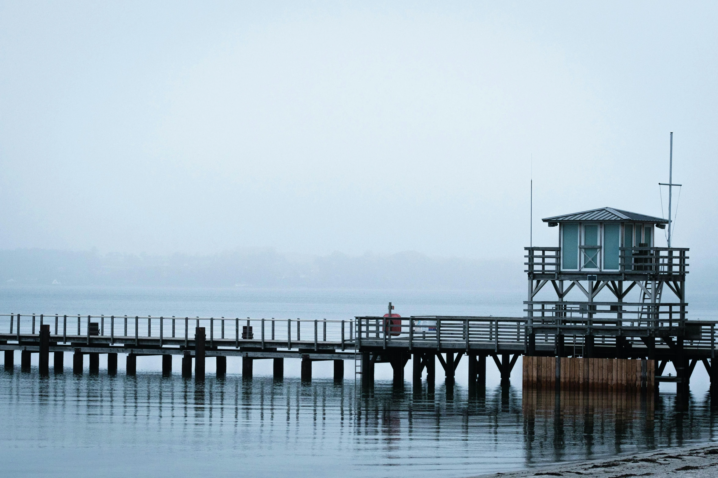 a man standing on top of a pier next to a body of water, by Peter Churcher, light morning fog, fishing town, distant photo