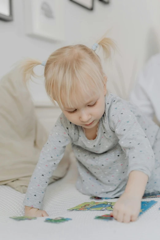 a little girl laying on a bed reading a book, a child's drawing, pexels contest winner, pastel coloring, blond boy, on grey background, babies in her lap