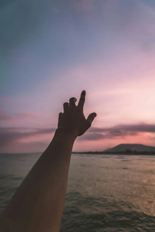 a person holding their hand up in the air over a body of water, pink skies, high-quality photo, middle finger, battered