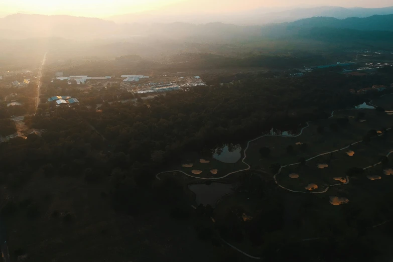 an aerial view of a golf course at sunset, by Adam Szentpétery, unsplash contest winner, sumatraism, soft light.4k, hideen village in the forest, movie still 8 k, distant mountains lights photo