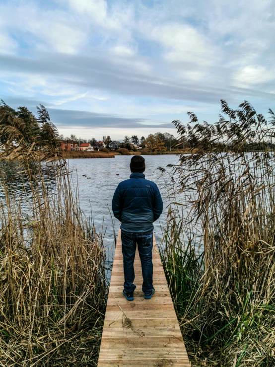 a man standing on a dock next to a body of water, a picture, by Sebastian Spreng, swedish countryside, phone photo, wideangle, college