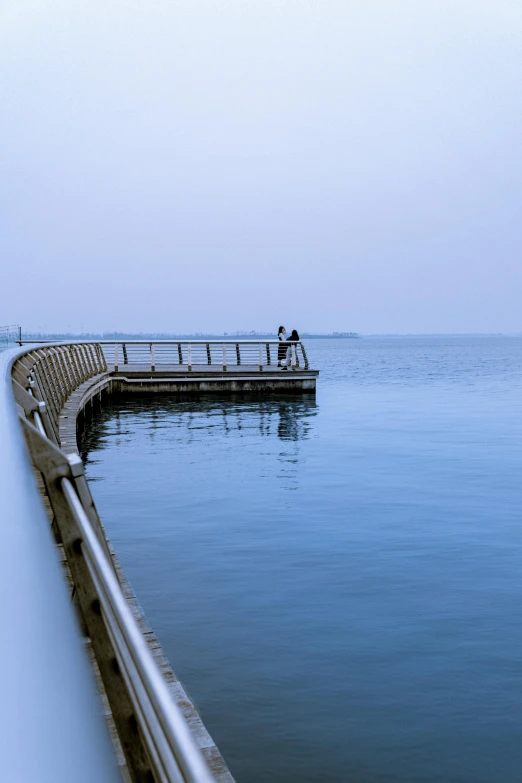 a man standing on top of a pier next to a body of water, by Okada Hanko, unsplash, pale blue fog, curved bridge, today\'s featured photograph 4k, benches