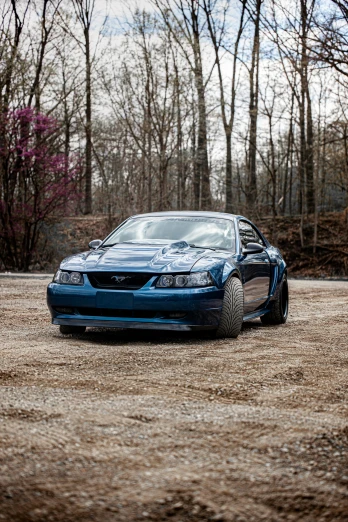 a blue car parked on top of a dirt road, a portrait, by Jeffrey Smith, unsplash, mustang, late 2000’s, modded, low profile