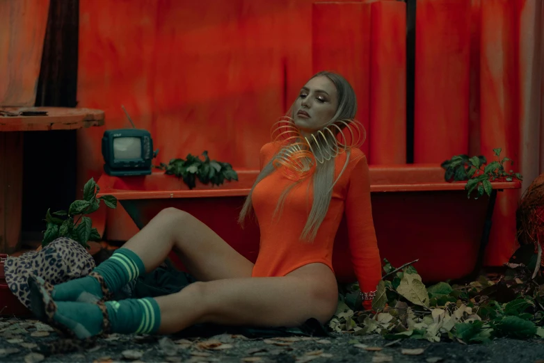 a woman in an orange bodysuit sitting on the ground, an album cover, inspired by Elsa Bleda, pexels contest winner, official music video, olya bossak, red neon details, a wide shot