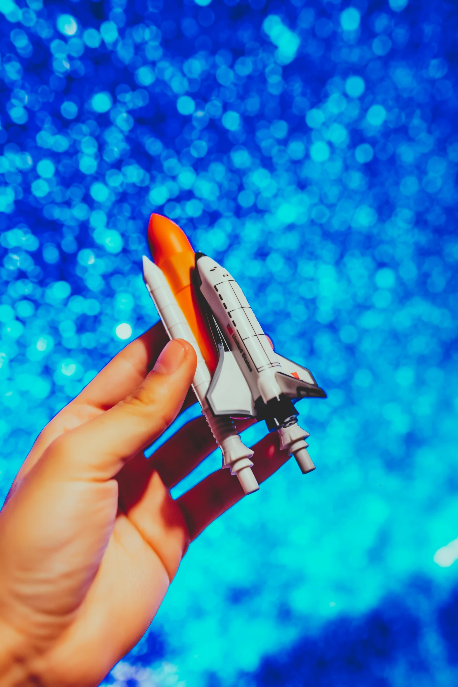 a person holding a space shuttle model in their hand, by Julia Pishtar, pexels contest winner, retrofuturism, blue background colour, swimming across the universe, concert, lush garden spaceship
