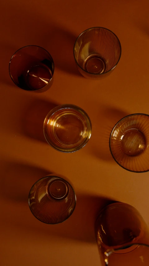 a group of glasses sitting on top of a table, a still life, by David Simpson, trending on unsplash, minimalism, glowing amber, close-up from above, drink, dynamic angled shot