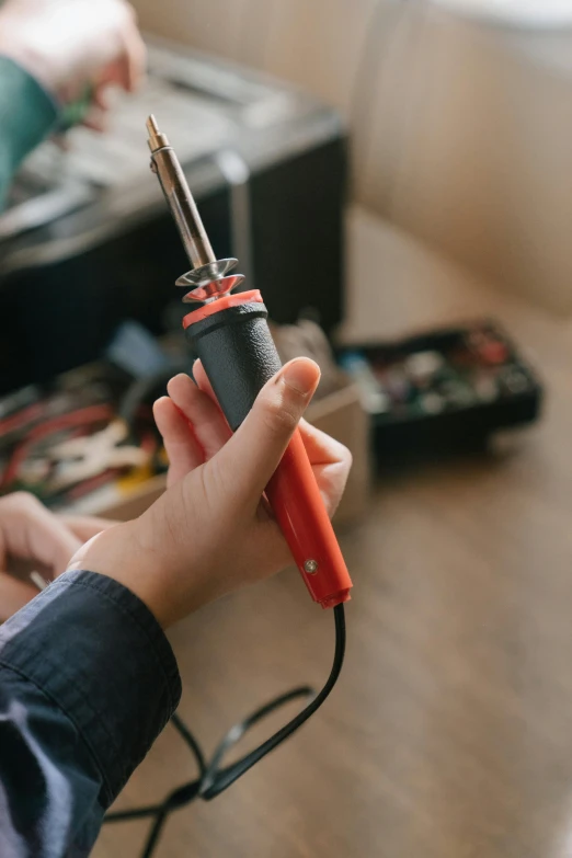 a person using a soldering tool on a table, holding it out to the camera, detailed product image, full color, cords