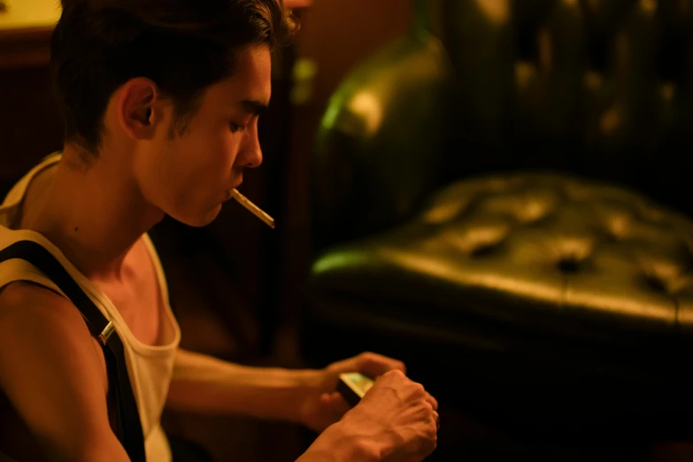 a man sitting on a couch with a cigarette in his mouth, inspired by Nan Goldin, pexels contest winner, cai xukun, sitting at the bar, ( ( theatrical ) ), robert sheehan