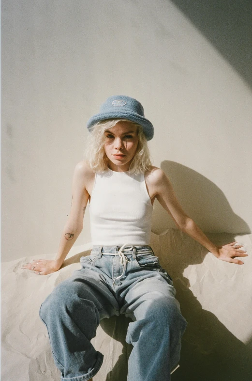 a woman sitting on top of a bed wearing a hat, inspired by Elsa Bleda, trending on pexels, baggy jeans, die antwoord yolandi visser, pale bluish skin, wearing a tanktop