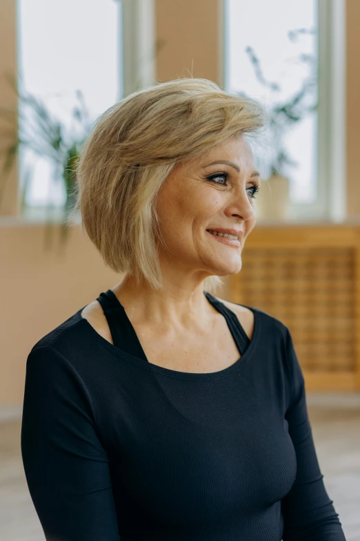 a woman in a black top sitting on a yoga mat, inspired by Judy Takács, arabesque, blond bob haircut, older woman, professional profile photo, turning her head and smiling