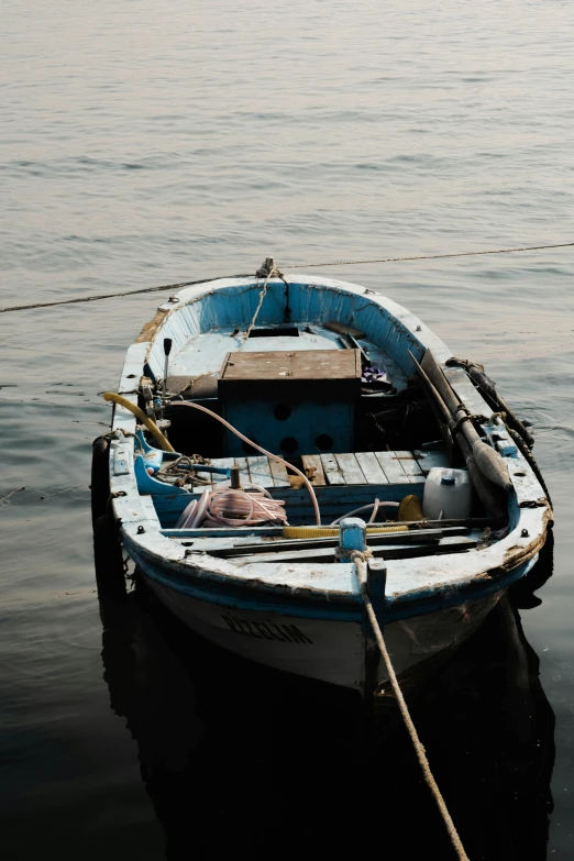 a blue and white boat sitting on top of a body of water, pexels contest winner, faded and dusty, an olive skinned, dark dingy, black sea