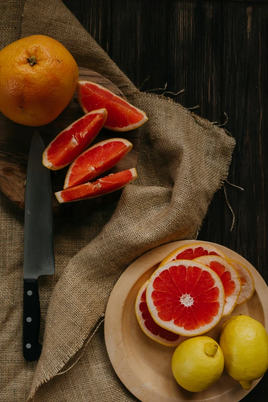 a plate of grapefruits next to a knife and some lemons, pexels contest winner, renaissance, a wooden, light red and deep orange mood, looking seductive, botanicals