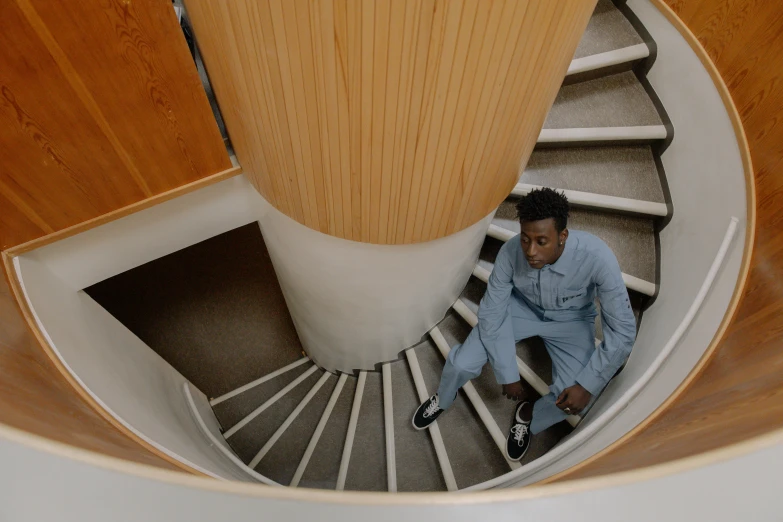 a man sitting on top of a spiral staircase, by Stokely Webster, looking down on the view, student, walking towards the camera, riyahd cassiem