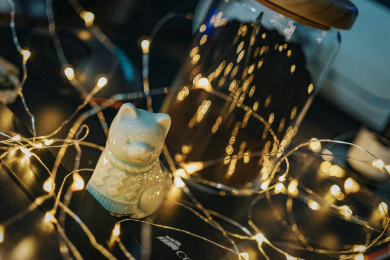 a cat figurine sitting on top of a table, pexels contest winner, arts and crafts movement, string lights, bubbly, high angle close up shot, cosy atmosphere