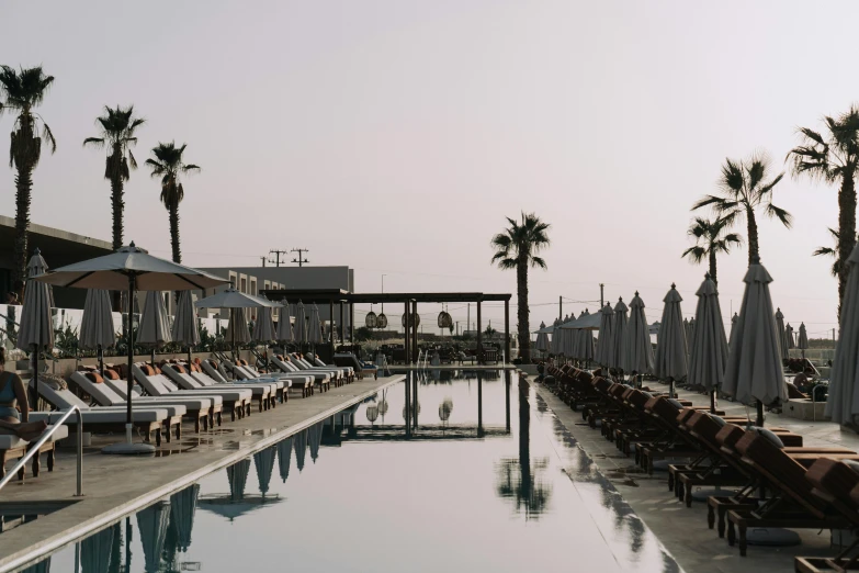 a pool filled with lots of lounge chairs next to palm trees, unsplash contest winner, cyprus, very hazy, conde nast traveler photo, city views