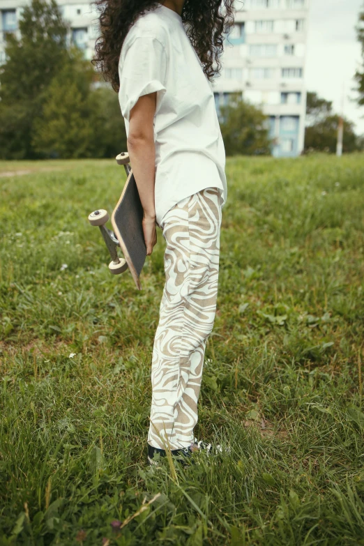 a woman standing in a field holding a skateboard, by Nina Hamnett, happening, white tiger, worn pants, subtle patterns, khakis