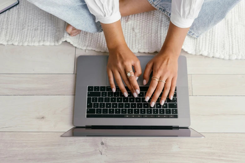 a close up of a person typing on a laptop, by Carey Morris, trending on pexels, sitting on the floor, flat lay, feminine looking, covered