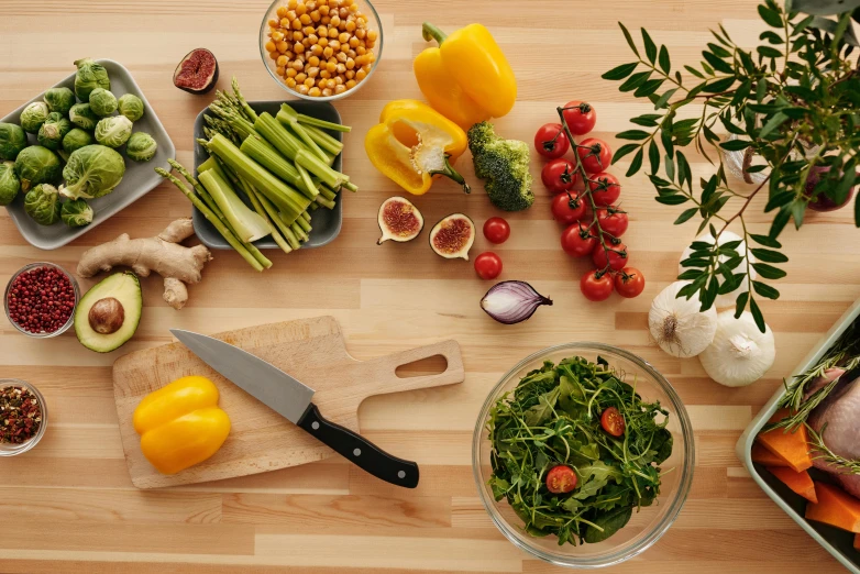 a wooden table topped with different types of vegetables, holding a kitchen knife, detailed product image, high quality product image”, lush greens