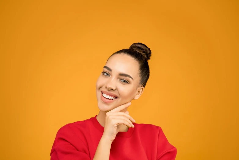 a woman in a red shirt posing with her hand on her chin, trending on pexels, antipodeans, hair styled in a bun, yellow-orange, smileing nright, manuka