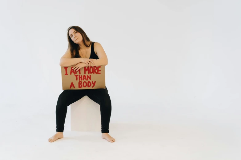 a woman holding a cardboard sign that says it's more than a body, pexels contest winner, sitting down, deformed human body, profile image, fit woman