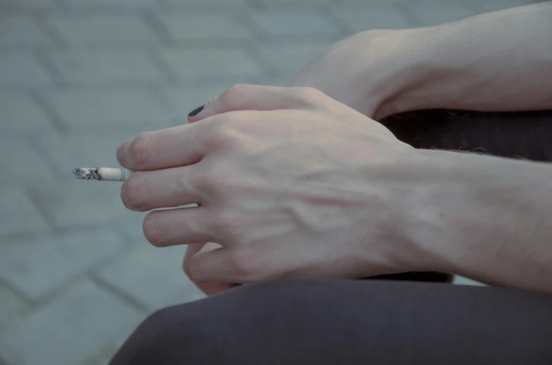 a close up of a person holding a cigarette, sitting down, ultrarealistic, ground - level medium shot, extremely pale