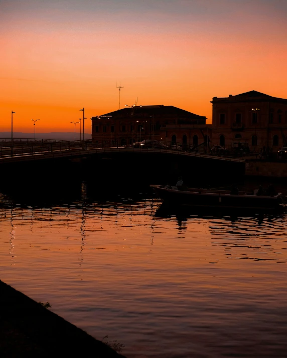 a couple of people standing next to a body of water, by Alexis Grimou, city sunset, thumbnail, low quality photo