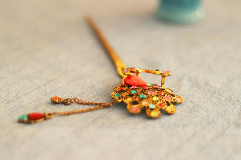 a close up of a necklace on a table, inspired by Tang Di, pink hair covered with hairpins, peacock, detailed product shot, rusty