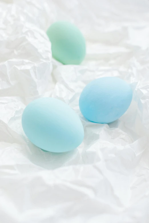 three blue eggs sitting on top of a white sheet, a pastel, trending on unsplash, colored gels, pastel green, matte finish, candy decorations