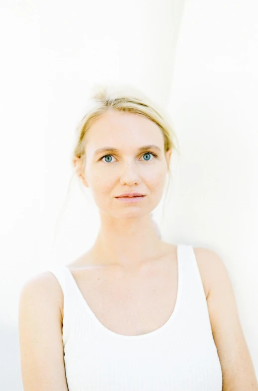 a woman standing in front of a white wall, by Ulrika Pasch, minimalism, headshot photo, yoga, midsommar style, diffused natural skin glow