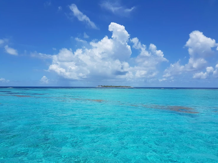 a large body of water with a small island in the distance, an album cover, pexels contest winner, carribean turquoise water, tropical reef, conde nast traveler photo, light blue sky